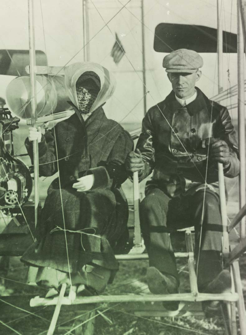 Katharine Wright and Wilbur Wright Preparing to Fly, Pau, France, February 15, 1909 Man in leather jacket and cap sits beside woman in hat, veil, and long coat among the structure of an apparatus