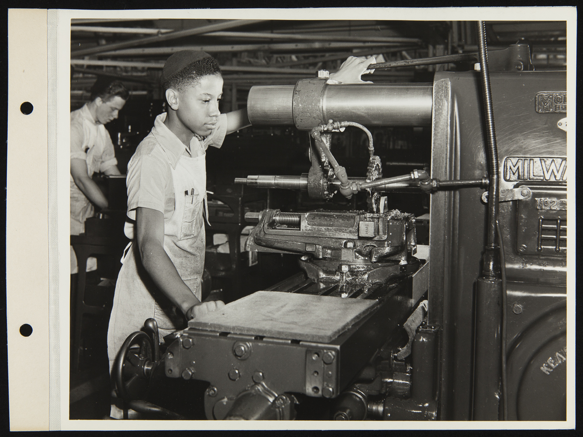 Trade School Student at the Ford Motor Company Rouge Plant, August 3, 1942 African American boy wearing apron and skullcap works at machine; another boy at another machine in background