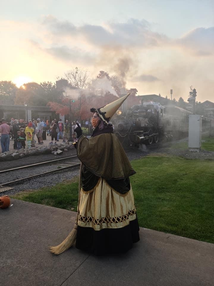 Woman in witch costume in front of a locomotive and crowd of people