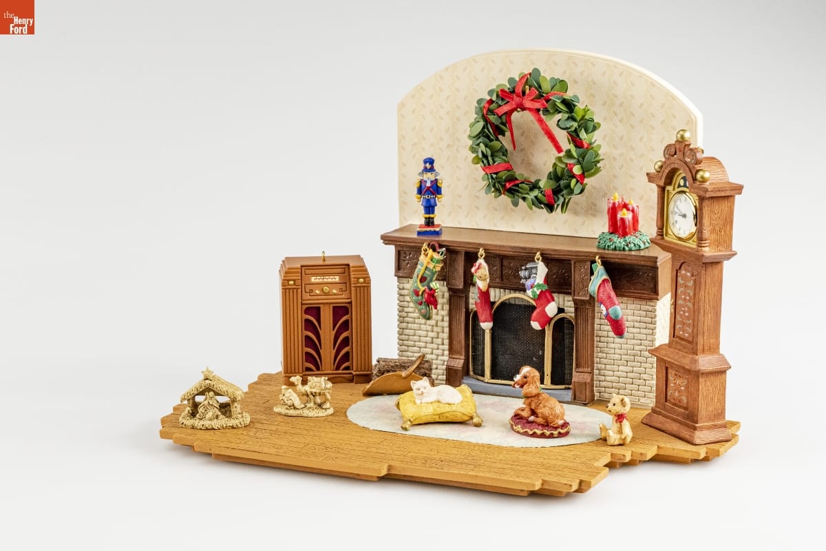 Hallmark "The Family Room" Studio Limited Edition Christmas Ornaments, Figurines and Base, 2002 Vignette of part of room, with stockings hung from mantel, a Christmas wreath above the fireplace, and a dog and cat lying on pet beds, as well as other furniture