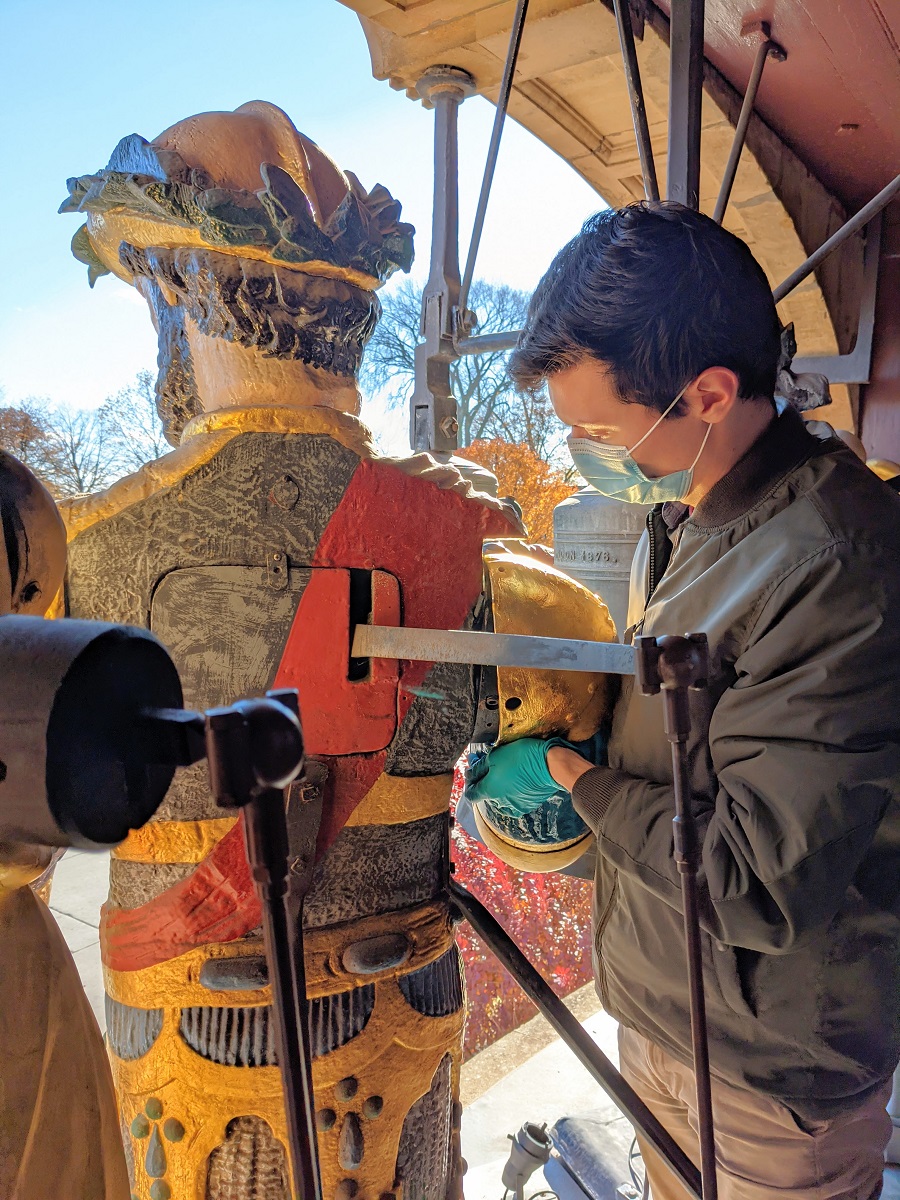 Andrew Ganem and Magog Person wearing mask holds a portion of a painted statue