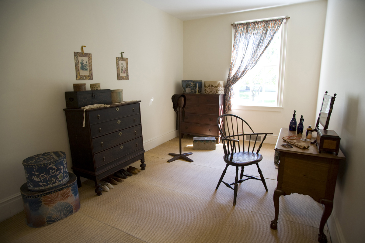 Narrow room with one window, chair and desk, two dressers, and other furnishings