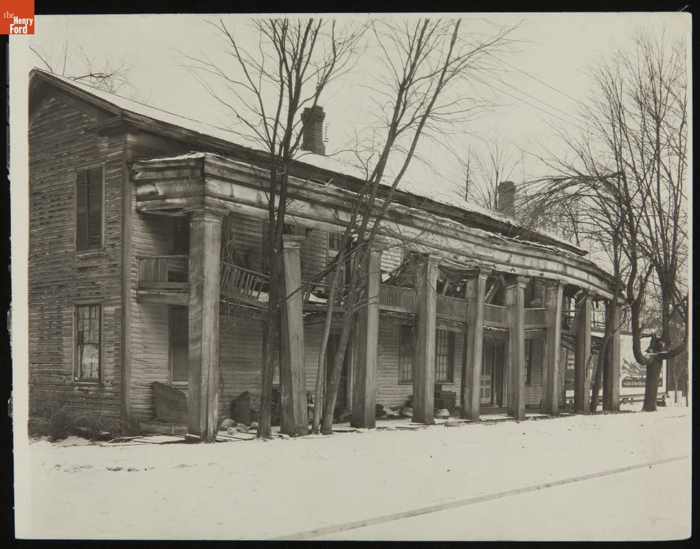 Decrepit two-story wooden building with columns in front, leaning at different angles, and second-floor balcony that is sagging  