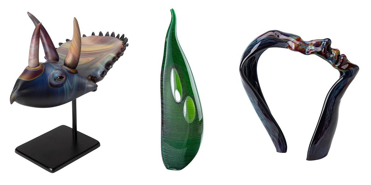 three glass sculptures, one resembline a dinosaur head, one green abstract shape, and one profile of a face with a hollow middle