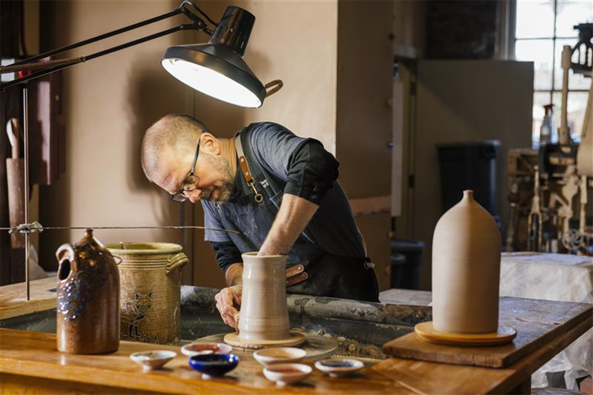 Artisan creating pottery in the Pottery Shop. Mini bowls made from extra clay and remnant glaze are in the foreground. / Image by The Henry Ford