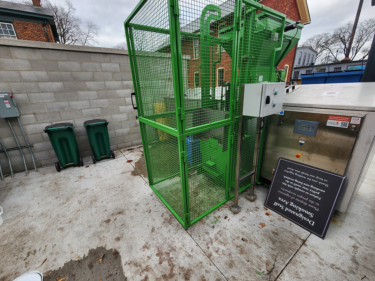 a green metal mesh cage outdoors on a stone patio