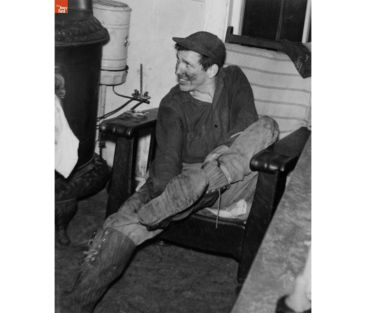 Bob Kelley removing his boots near the heating stove in the Kelley house kitchen, Rockville, Connecticut, 1948 / THF723649