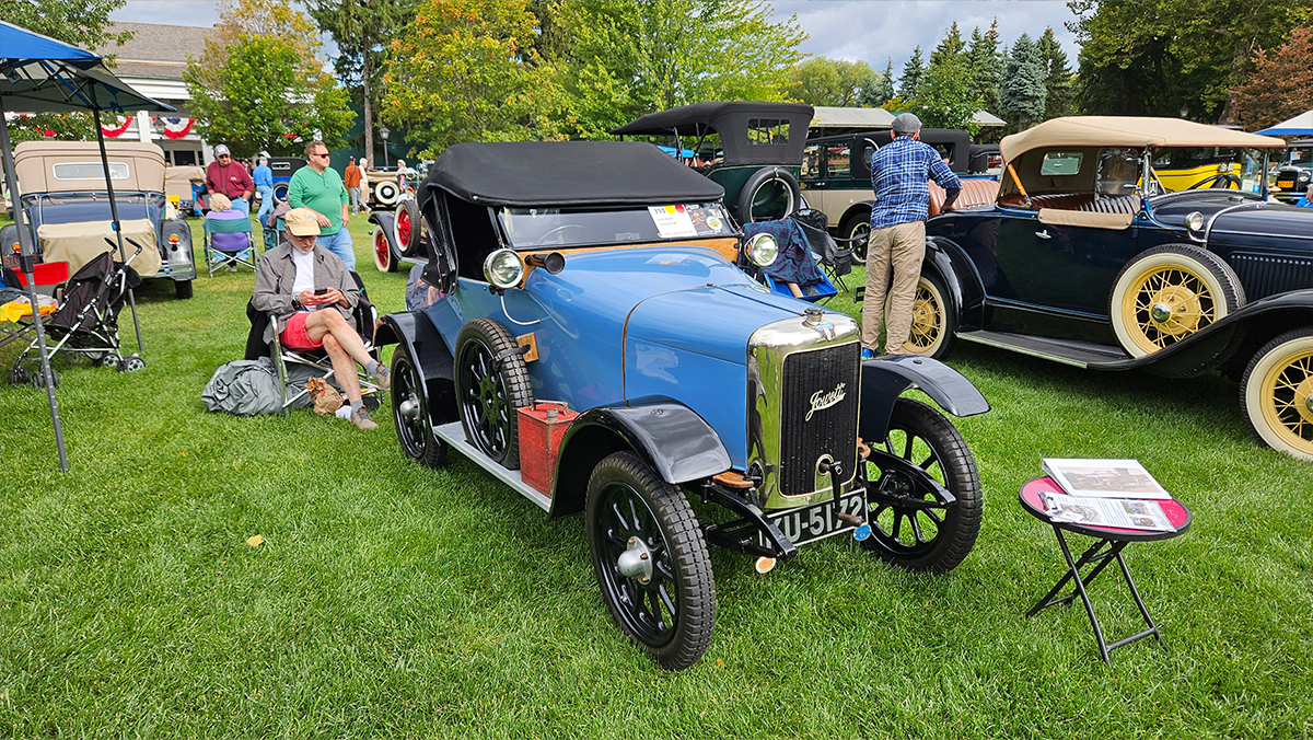 a blue 1924 Jowett parked in a field with other antique vehicles