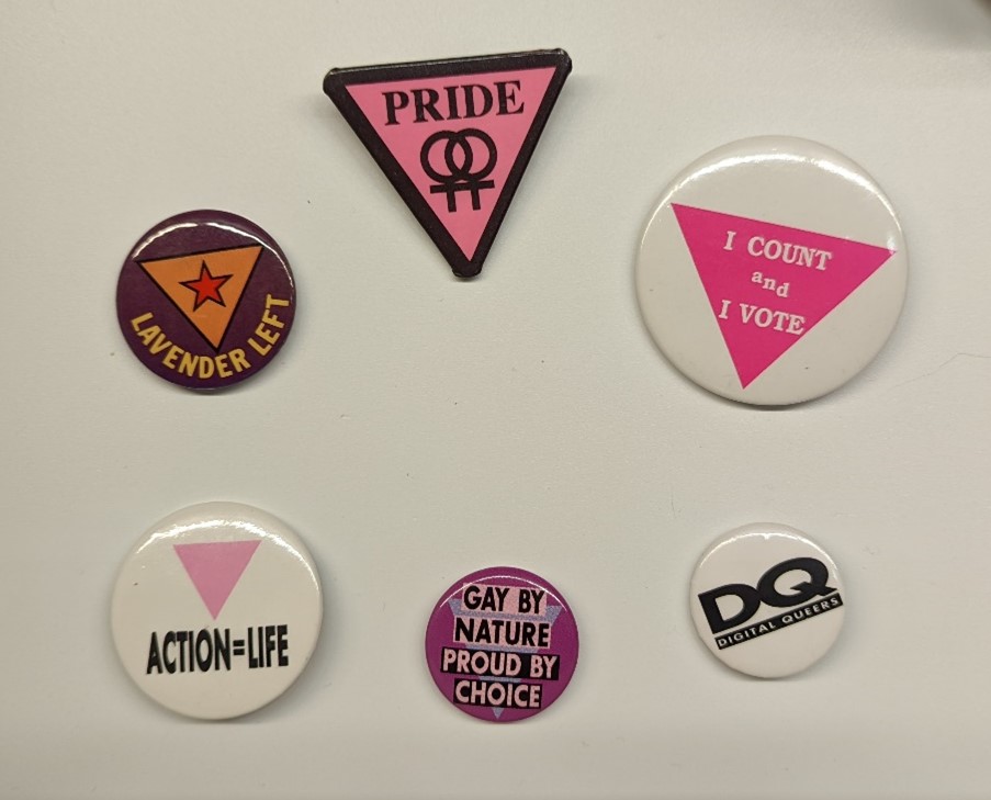 Six pins/buttons with text related to LGBTQ+ issues, most also featuring triangles
