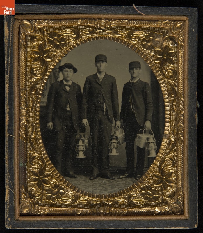Intricate gold frame with black-and-white image of three men in suits and hats holding lanterns and lunch pails 