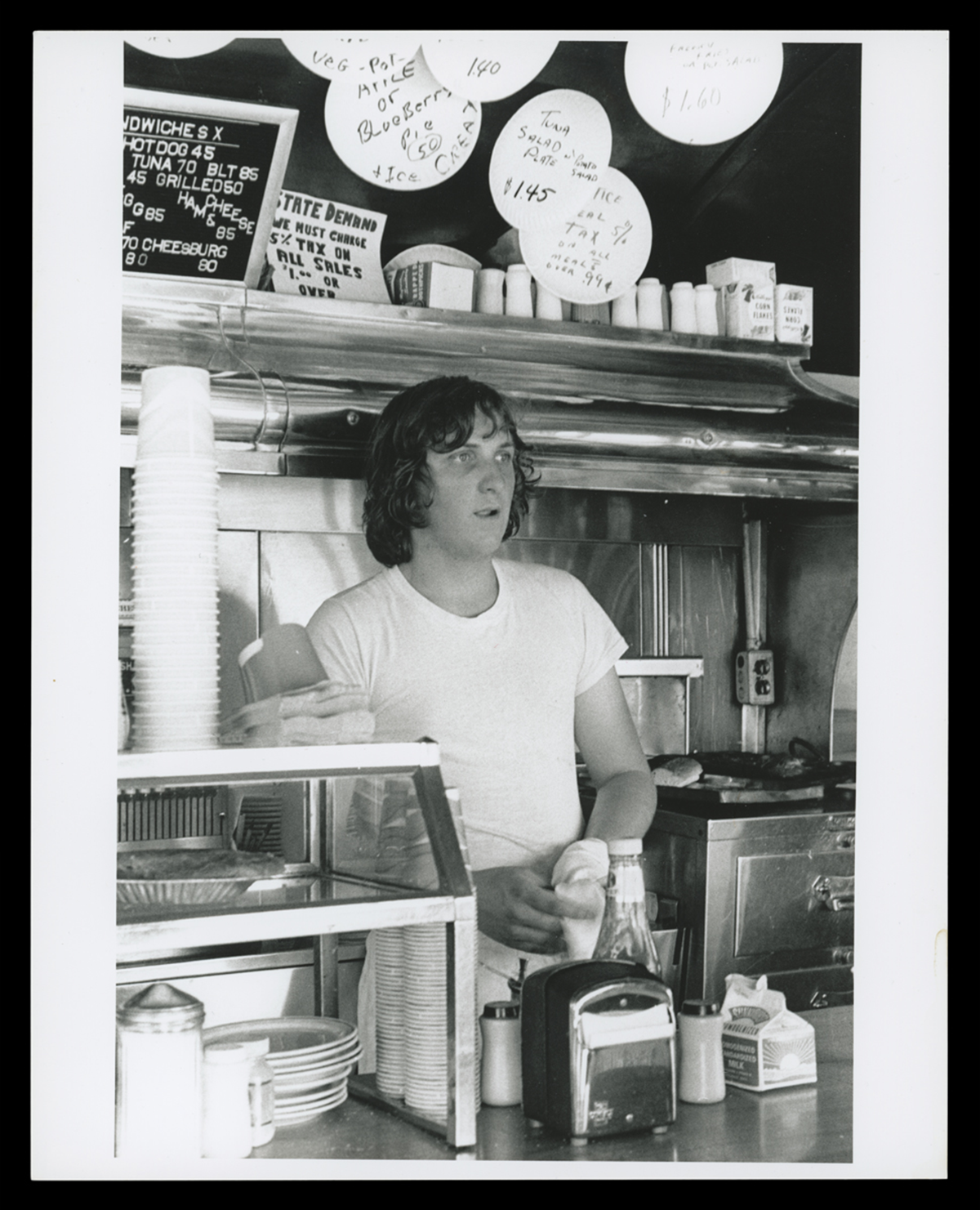 Cook Kenny Barrett inside Buddy's Truck Stop, Somerville, MA, circa 1974. Note the handwritten specials on paper plates.
